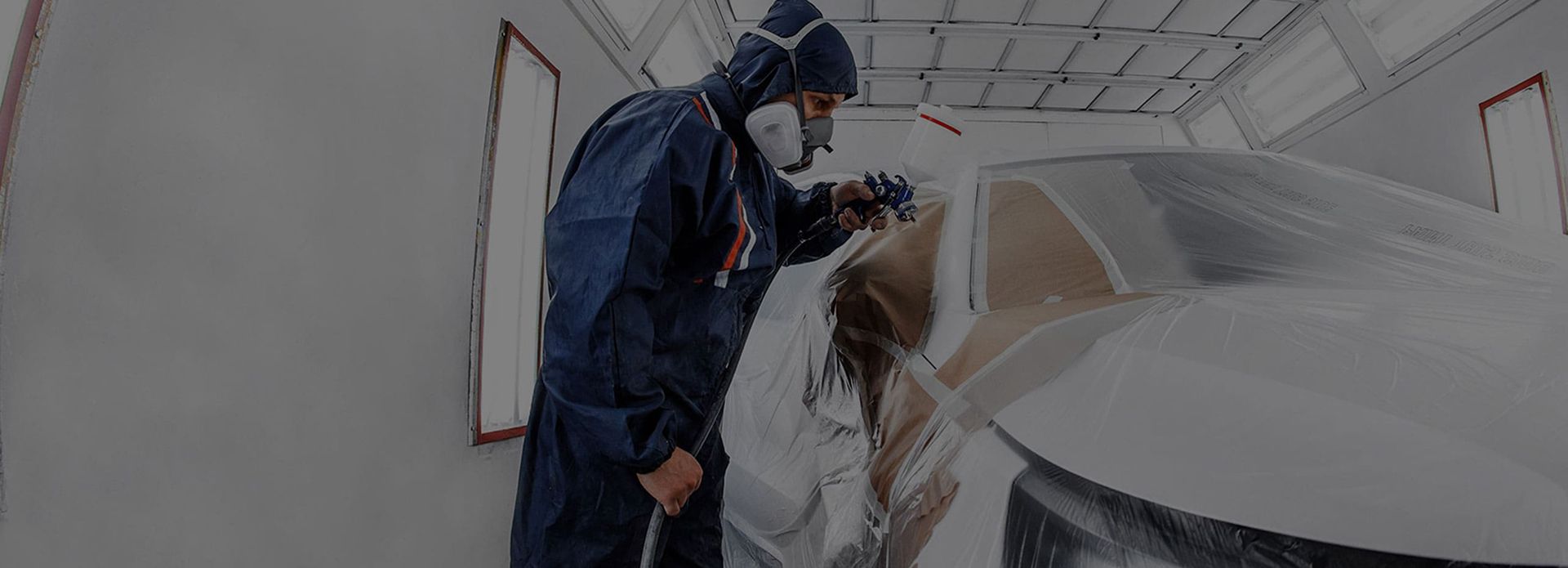 Mann besprüht in einem blauen Overall ein Auto